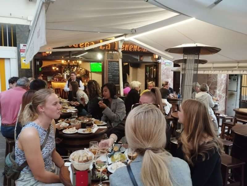 Groep mensen eet en praat bij een drukke buitenbistro.