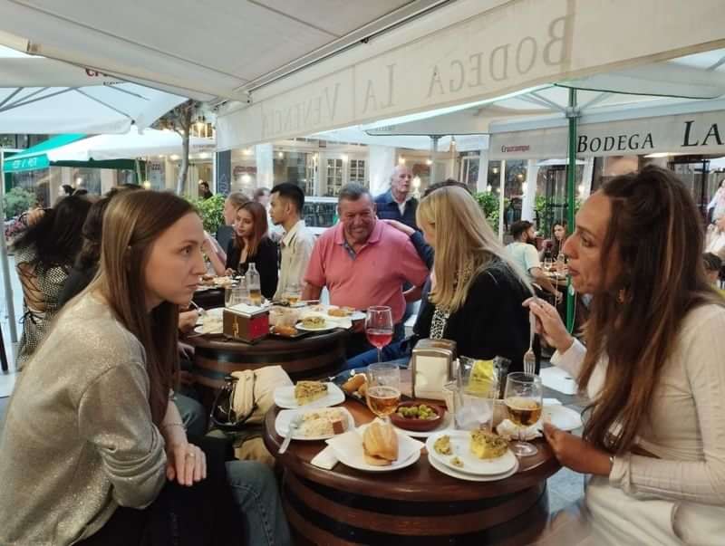 People enjoying outdoor dining at a Spanish bodega, conversing and eating tapas.