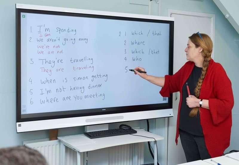 Teacher instructing English grammar, focusing on present continuous and question words.