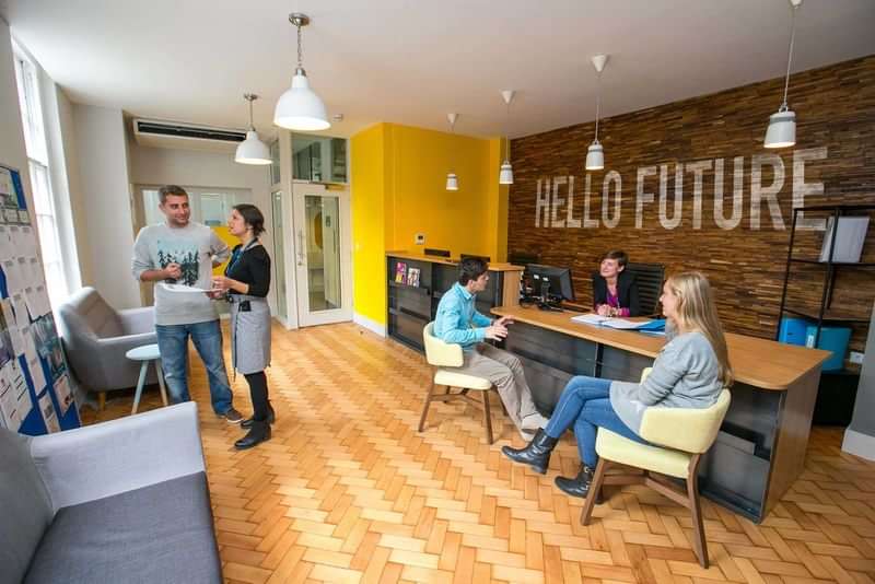 Language school reception area with students, "Hello Future" sign on wall.