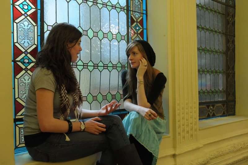 Two women conversing, likely practicing a language in a cultural setting.