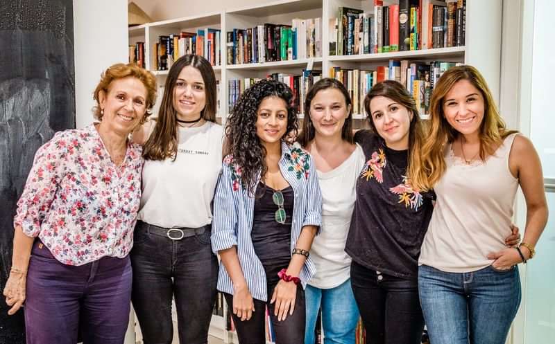 Groep vrouwen in een taalschool, boekenplanken op de achtergrond.