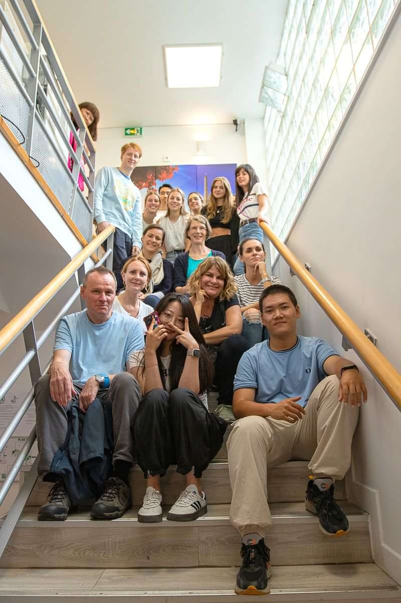 Groepsfoto van taalcursusdeelnemers, diverse nationaliteiten, op een trap binnen.