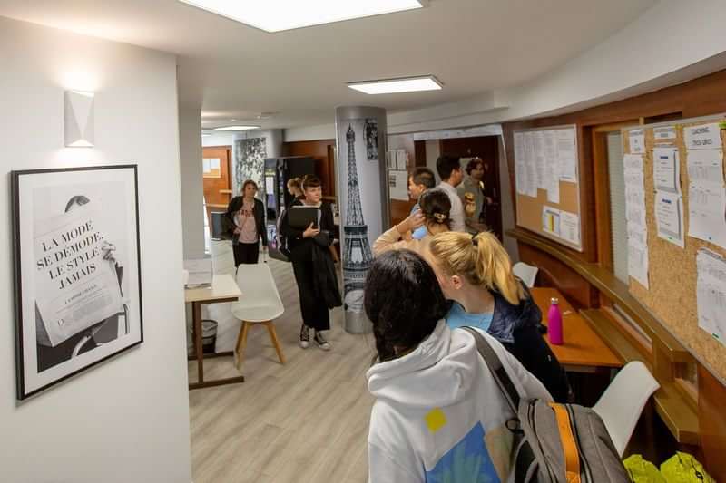 Students gathering in a language school, Eiffel Tower poster on wall.