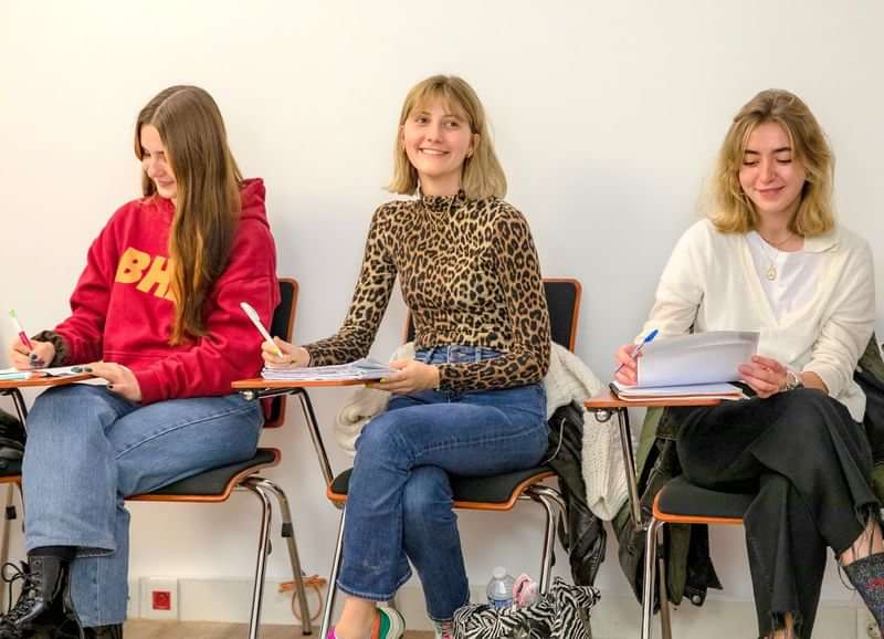 Students in a language class, smiling and writing notes.