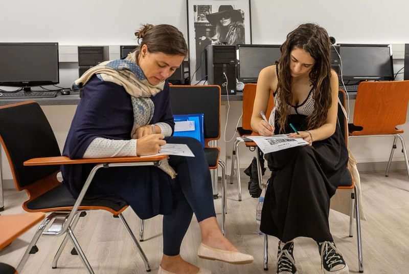 Two women learning a language together in a classroom setting.