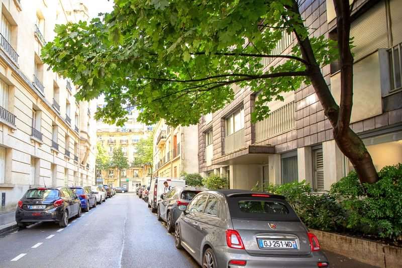 Straat met geparkeerde auto's, bomen en gebouwen in een stad.