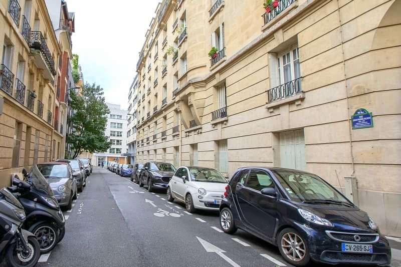 Een smalle straat met geparkeerde auto's en gebouwen aan weerszijden.