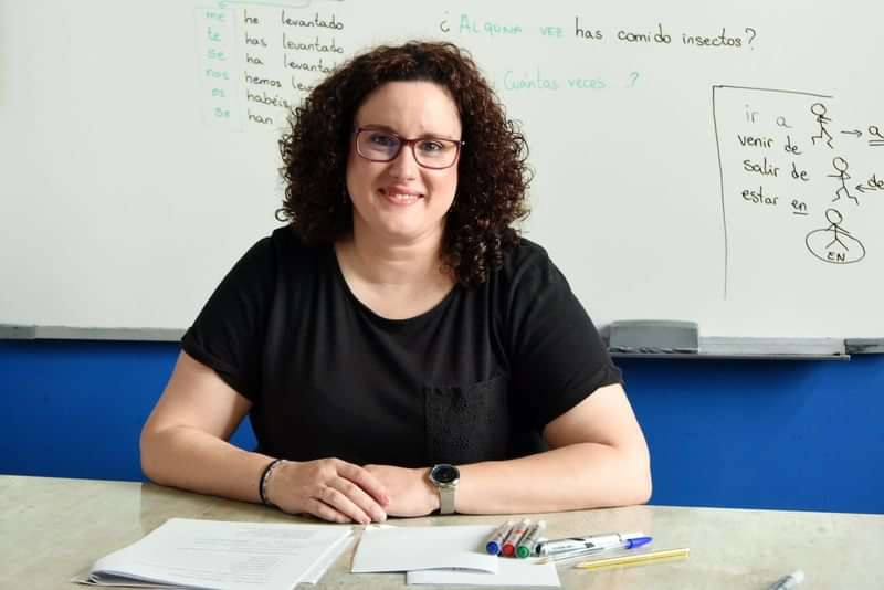 Woman teaching language concepts in a classroom, whiteboard with notes.