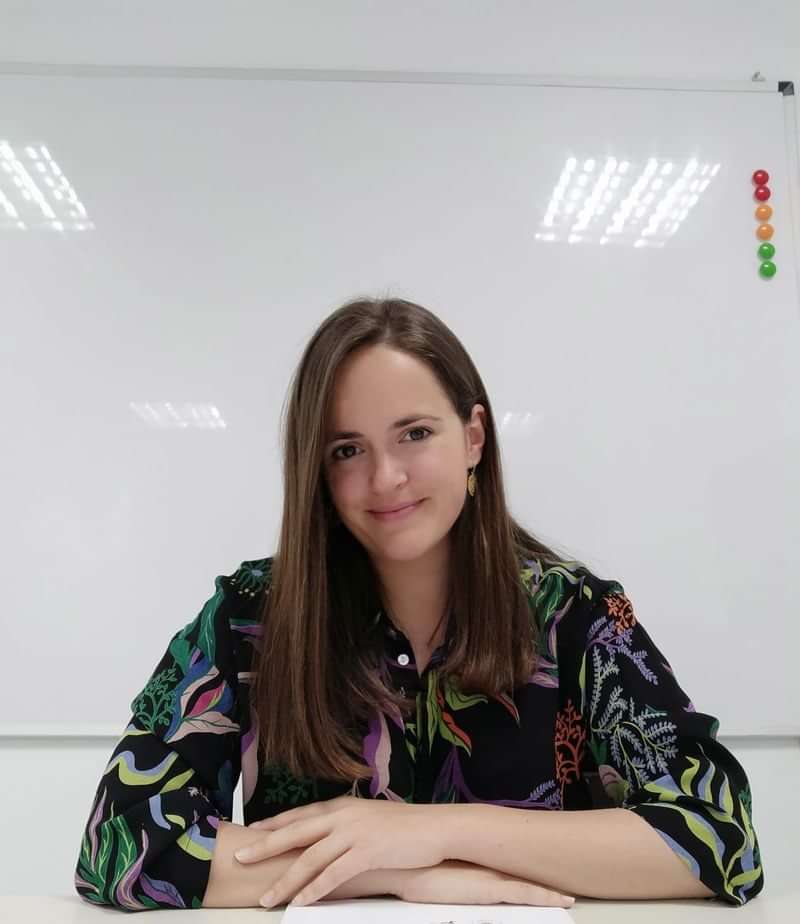 A language teacher smiling in a classroom, ready for a lesson.