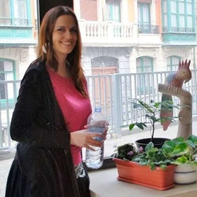 Woman watering plants by a window in a vibrant city setting.