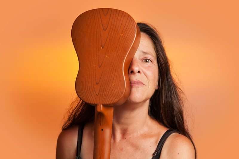 Een vrouw met een gitaar tegen haar gezicht.