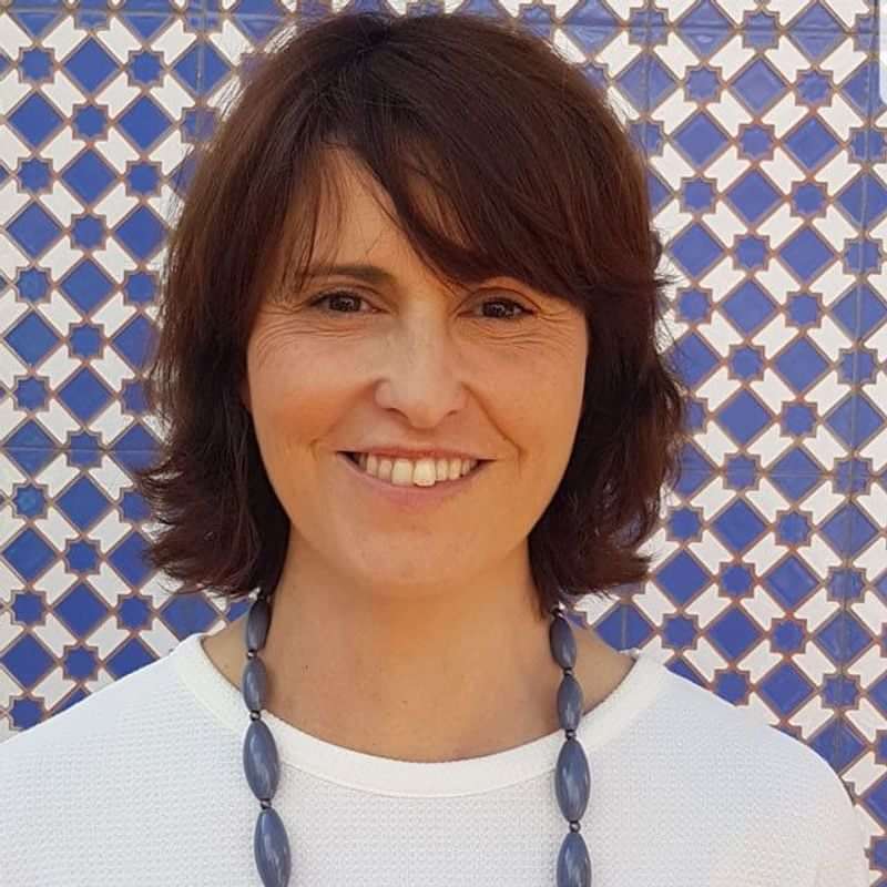 Smiling woman, blue-patterned backdrop, ready to teach language or explore culture.