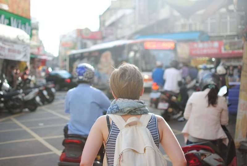 Een reiziger verkent een drukke stad, veel scooters en mensen.