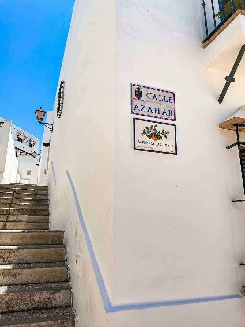 Street signs in Spanish, stairway, white buildings, clear blue sky.