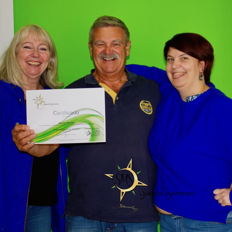 A man holding a Spanish language course certificate, smiling with teachers.