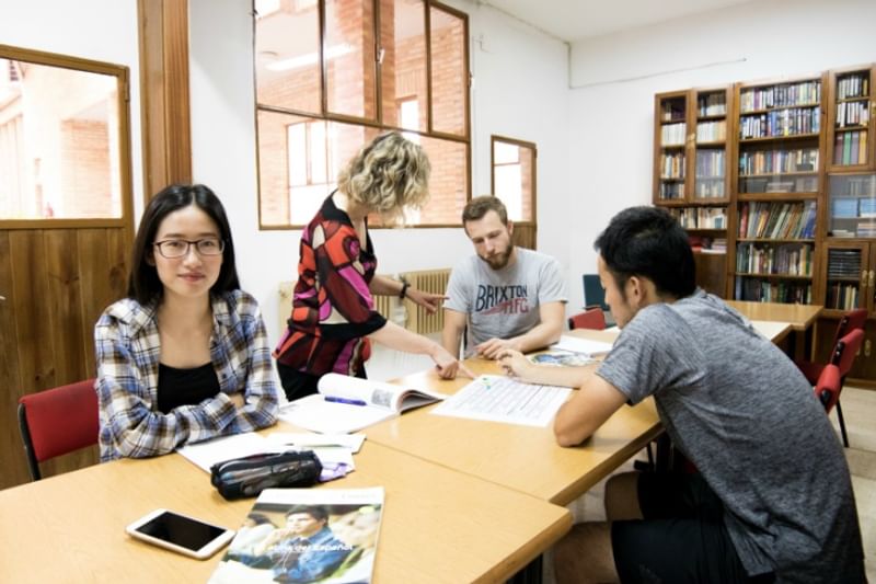 Taalstudenten studeren samen met een leraar in een bibliotheek.