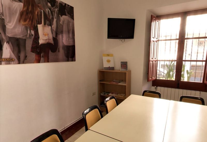 Klaslokaal voor taalreizen met tafel, stoelen, raam, bord en boekenplank.