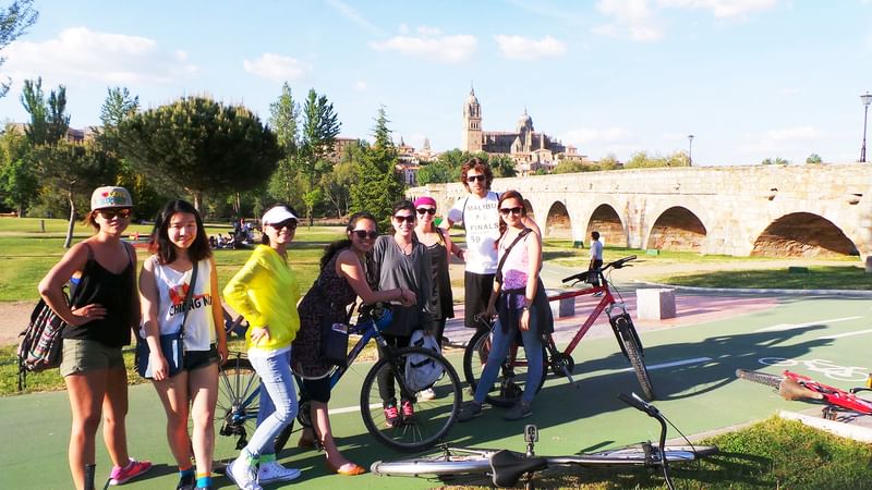 A group enjoying a biking tour near historic bridge, sunny weather.