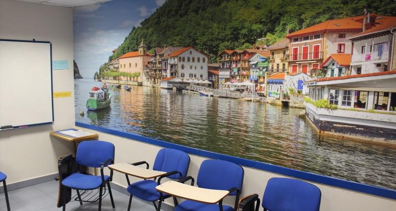 Classroom with chairs, desks, whiteboard, and mural of a scenic town.