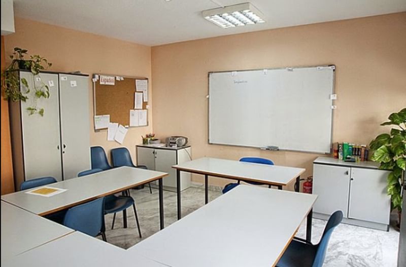 Een klaslokaal voor taalonderwijs met tafels, stoelen en een whiteboard.