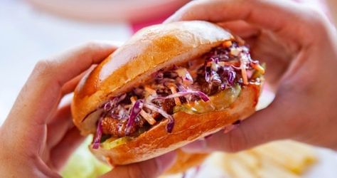 Two hands holding a sandwich with slaw and sauce between a bun							