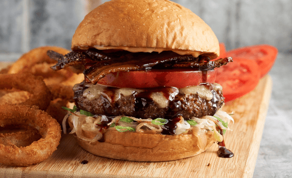 Big baller burger with a side of onion rings on a wood cutting board