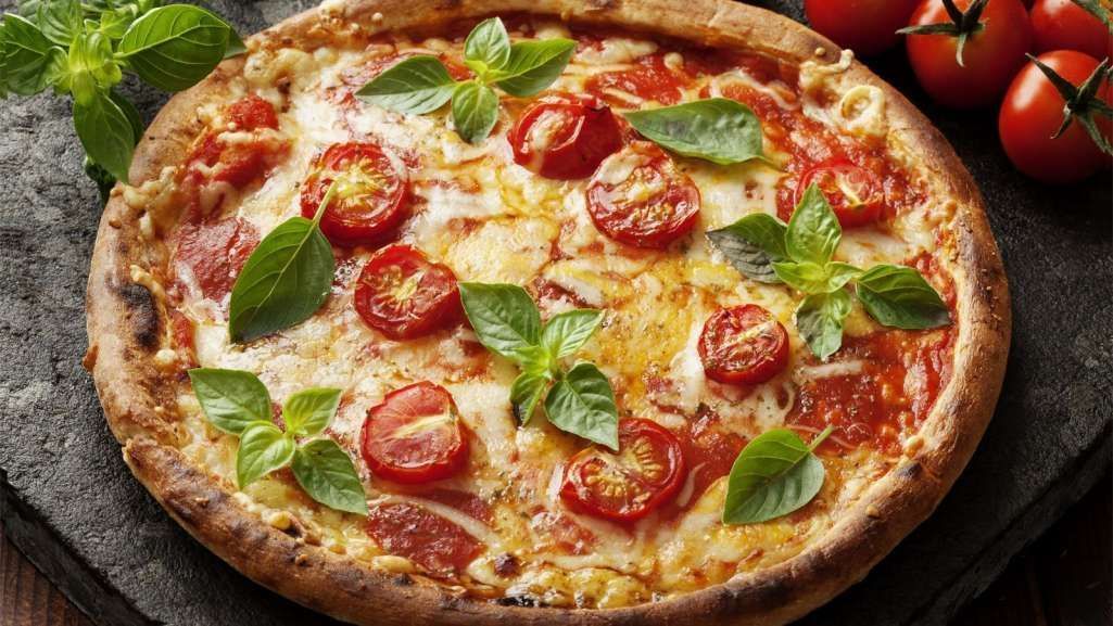 Pizza de queijo com tomates pequenos e folhas de manjericão.