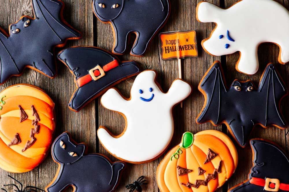 Cookies de Halloween em formatos diversos como morcego, gatinho preto, fantasminha e abóbora decorada.