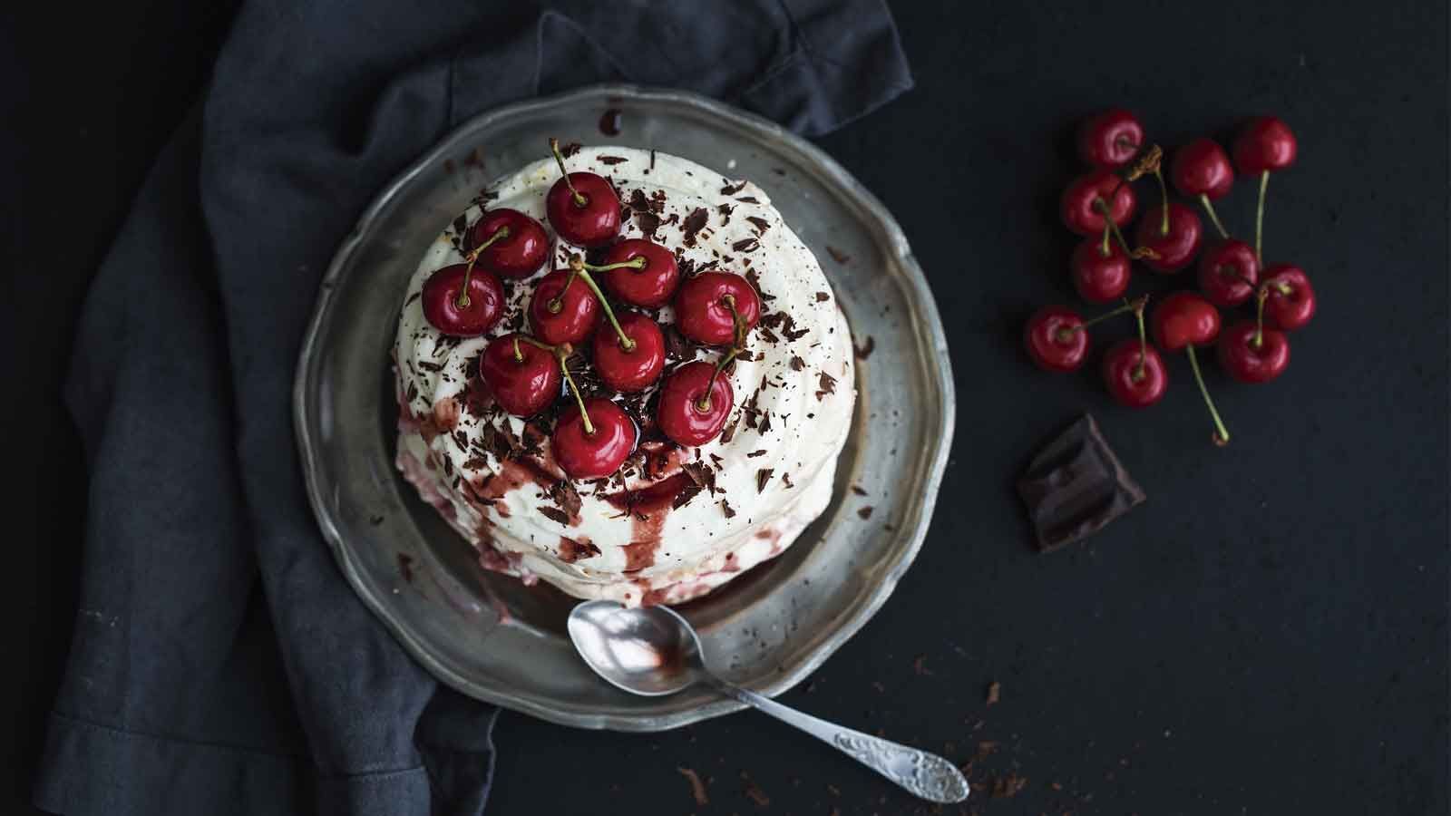 Receitas Batedeira Planetária - Pavalova em tigela. O doce tem cerejas vermelhas em cima de chantilly branco.