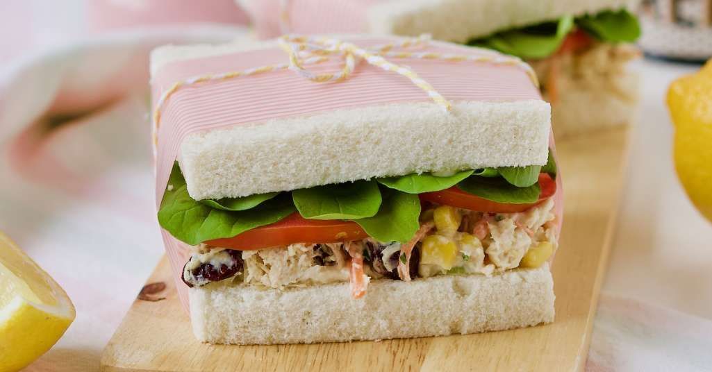 Sanduiche de pão branco com salpicão de frango desfiado e salada de folhas verdes.