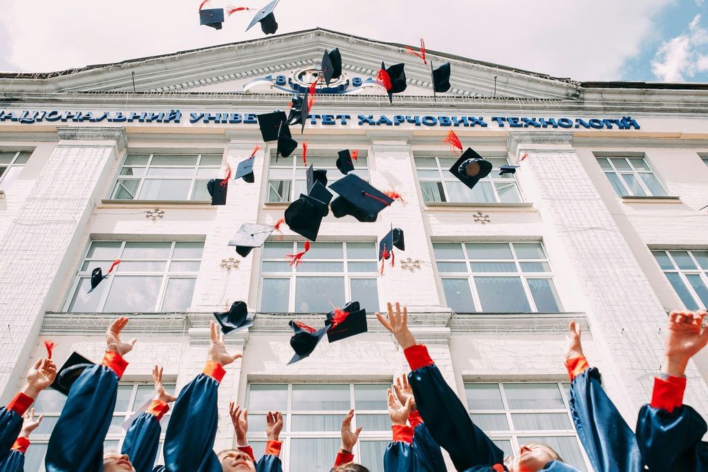 Estudantes comemorando a formatura e jogando o capelo para o alto.