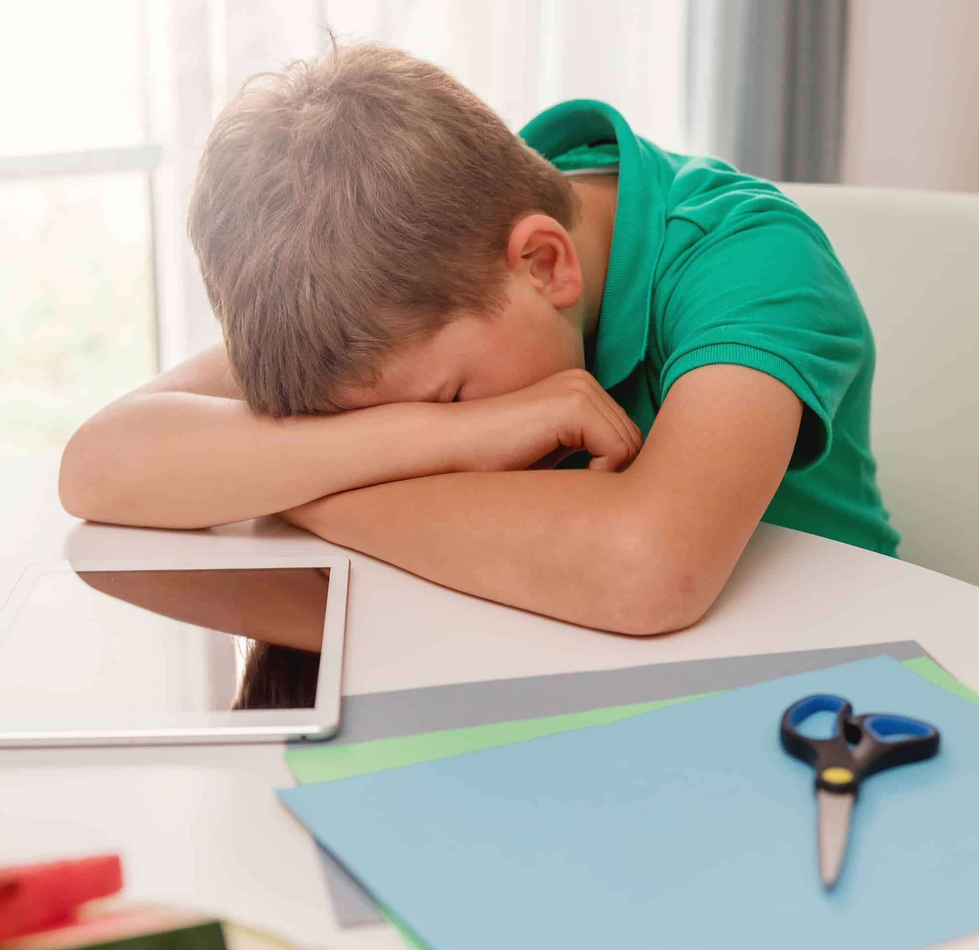 Menino deitado com a cabeça na mesa parece desmotivado, um dos principais sintomas de problema de aprendizagem.