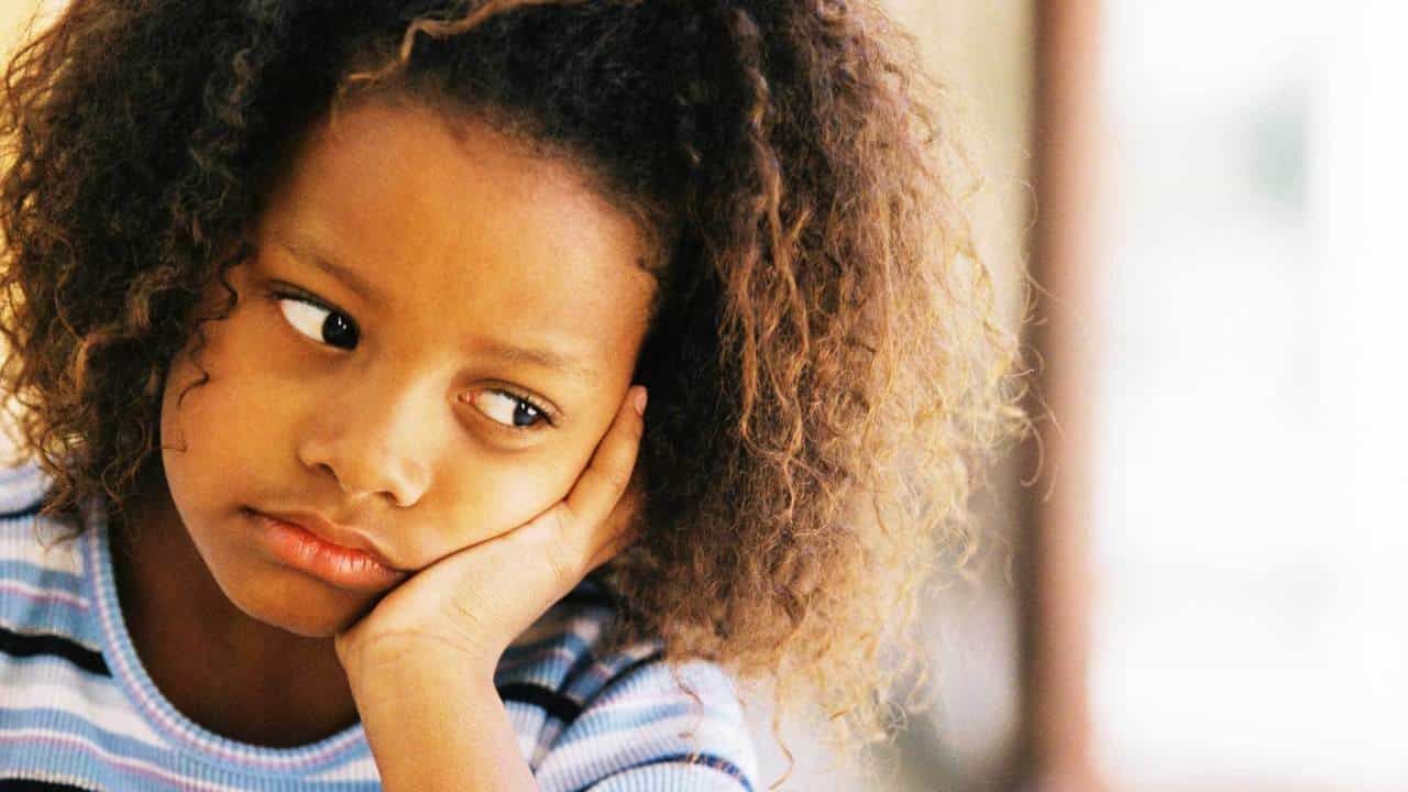 A imagem mostra uma criança negra com a mão no rosto, que parece triste. Tristeza excessiva é um dos sintomas que podem indicar um desequilíbrio emocional.