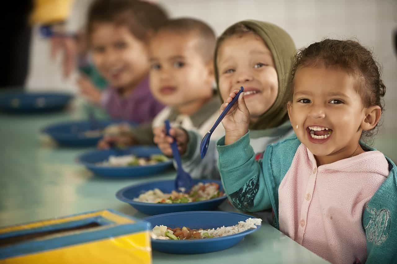 Crianças da creche Centro de Educação Infantil Professor Paulo Cesar dos Santos Mortari sentadas em uma mesa, almoçando. 