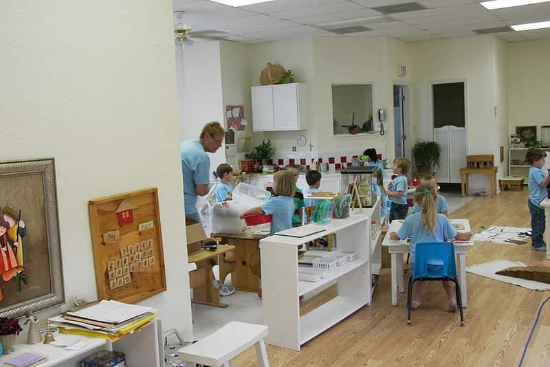 Crianças brincando sentadas em mesas brincando. A liberdade é uma das principais características do método Montessori.