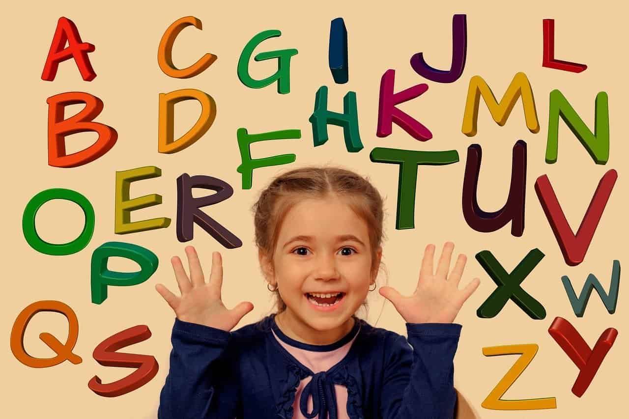 Criança com as mãos pra cima com as letras do alfabeto ao seu redor. Hoje, a tecnologia possibilitou que os professores usem jogos de alfabetização para os alunos aprenderem.