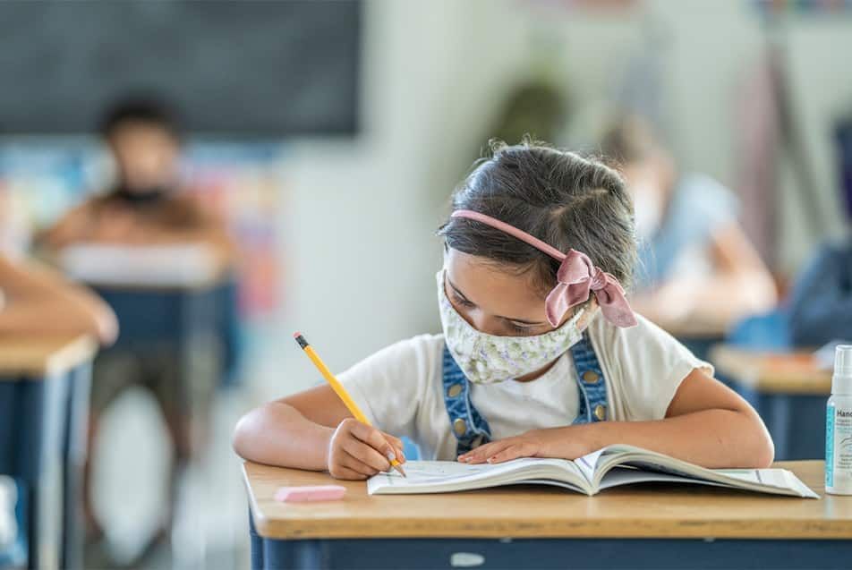 Menina usando máscara sentada na carteira da sala de aula. Além dos protocolos sanitários as escolas terão que utilizar estratégias de aprendizado para dar seguimento aos conteúdos no ano letivo de 2021.