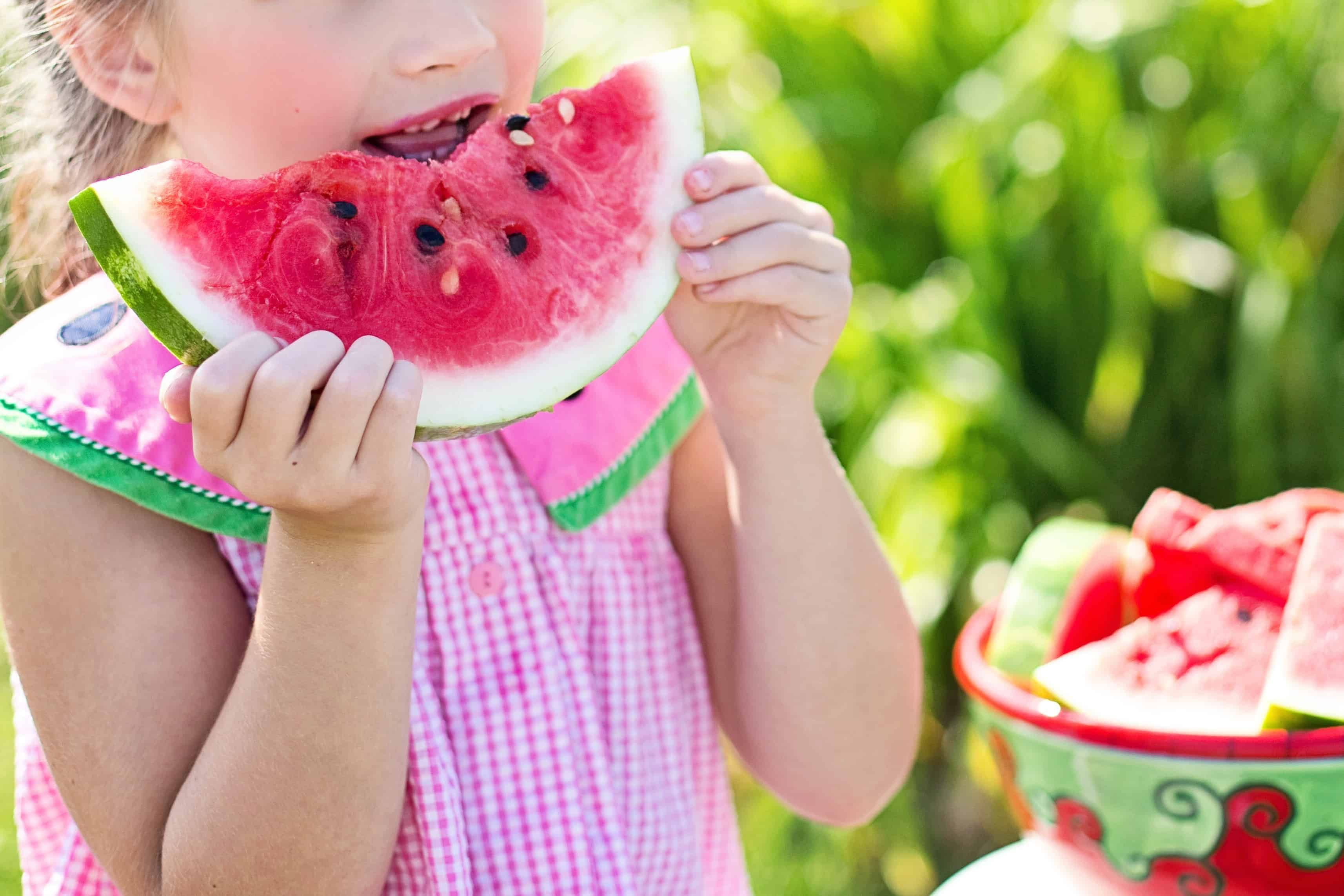 Menina loira comendo um pedaço de melancia, alimento natural que ajuda a aumentar a imunidade infantil.