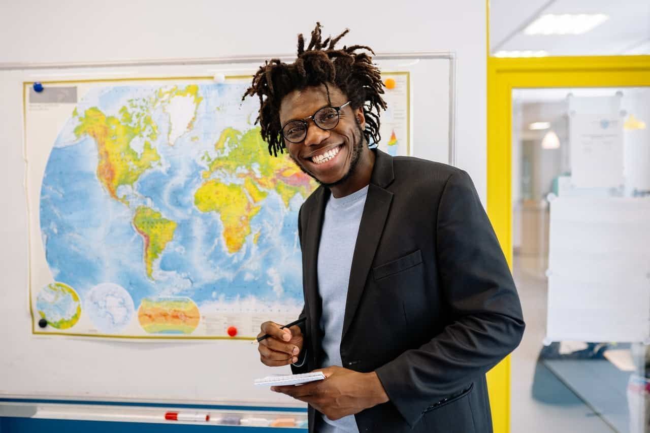 mensalidade de pedagogia professor negro dá aula com mapa mundi no fundo