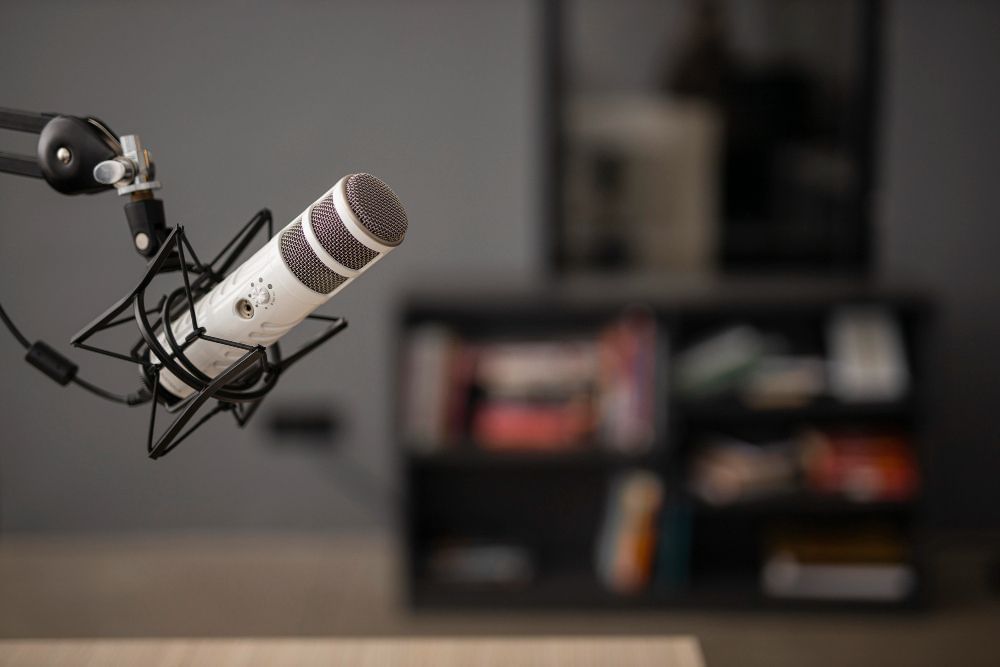 Imagem apresenta microfone utilizado para gravações de áudio e programas de podcast. Em segundo plano, um móvel é observável na imagem.