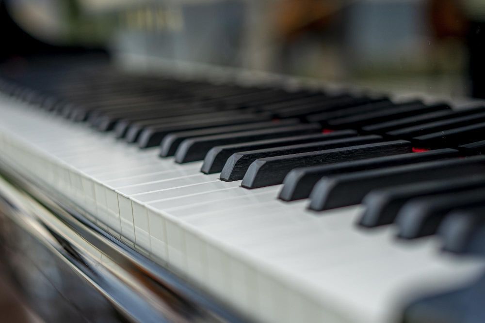 Imagem apresenta um piano como foco em suas teclas que estão em primeiro plano e, no fundo desfocado,  a estrutura do instrumento musical.