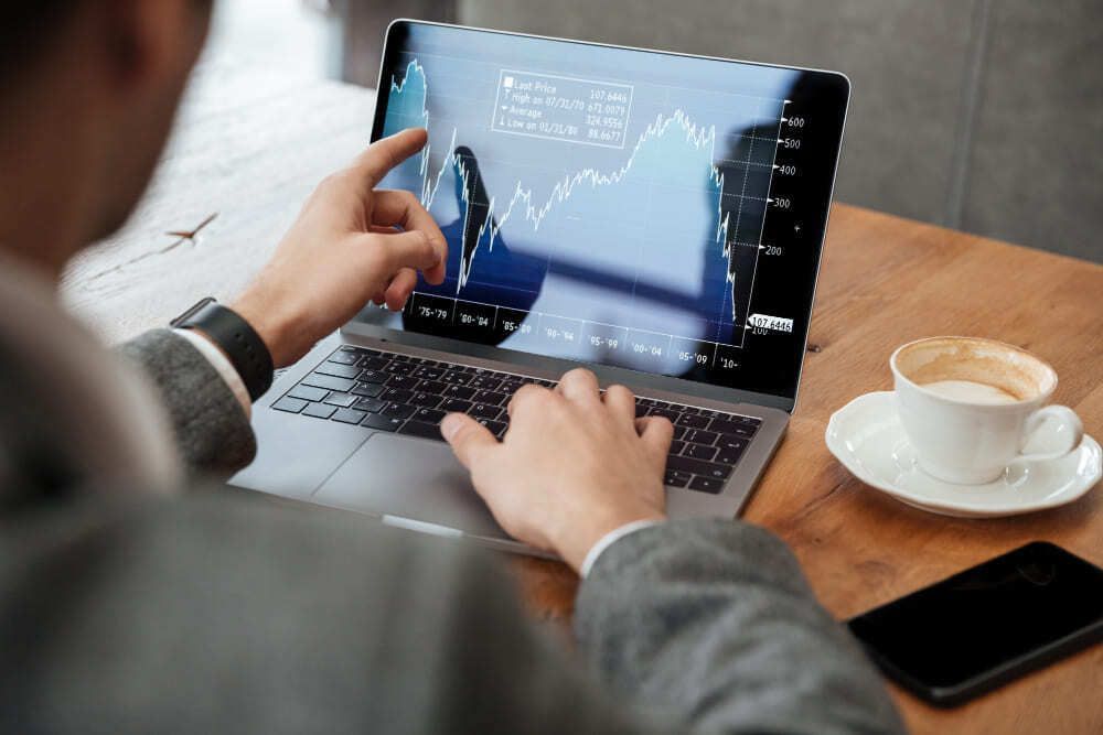 Pessoa observa gráficos e linhas referentes ao movimento do mercado financeiro que estão projetados em tela de computador. 
