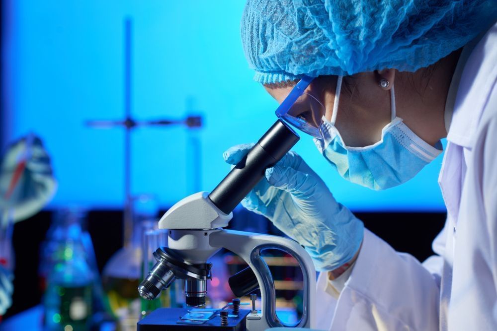 A imagem expõe uma profissional da área da Biomedicina utiliza microscópico para atuação profissional.