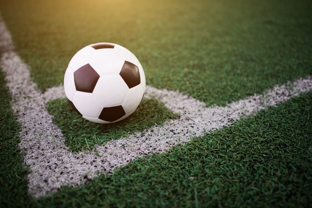 Imagem aponta bola de futebol parada em marca de escanteio de um campo de futebol.