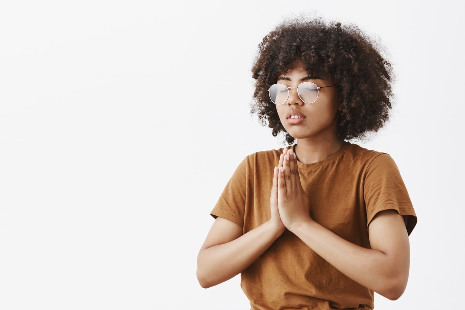 Jovem mulher com camiseta bege em fundo branco com mãos juntas rezando; Enem: 5 dicas para manter a saúde mental e não surtar