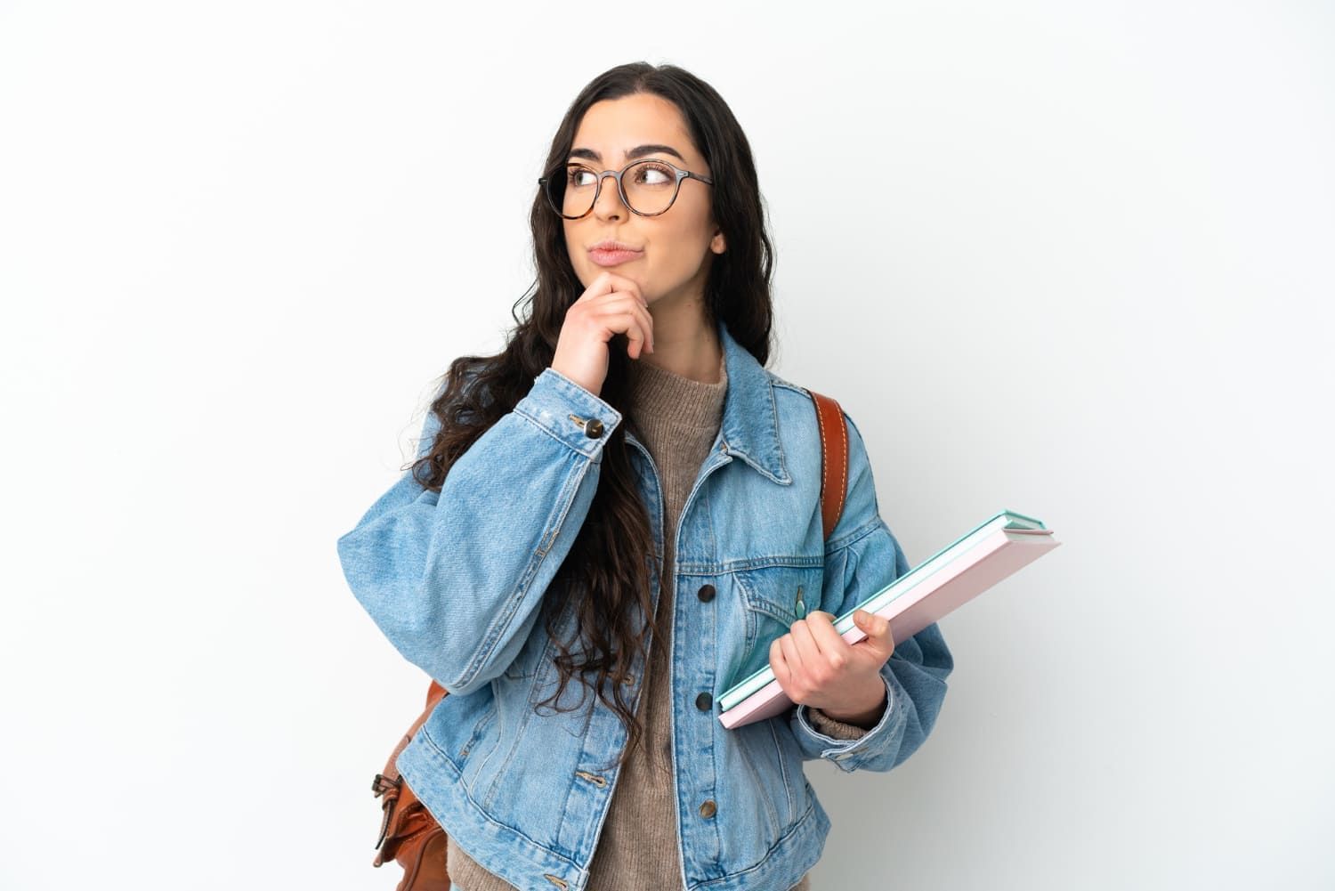 Jovem mulher estudante segurando cadernos com uma cara de dúvida; folga no dia do Enem: saiba como justificar falta no trabalho