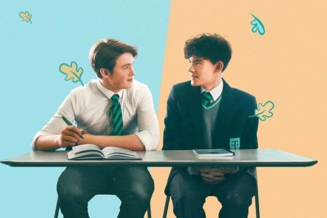 A imagem apresenta os personagens Nick e Charlie da série Heartstopper sentados em suas mesas da escola,na capa original da Netflix
