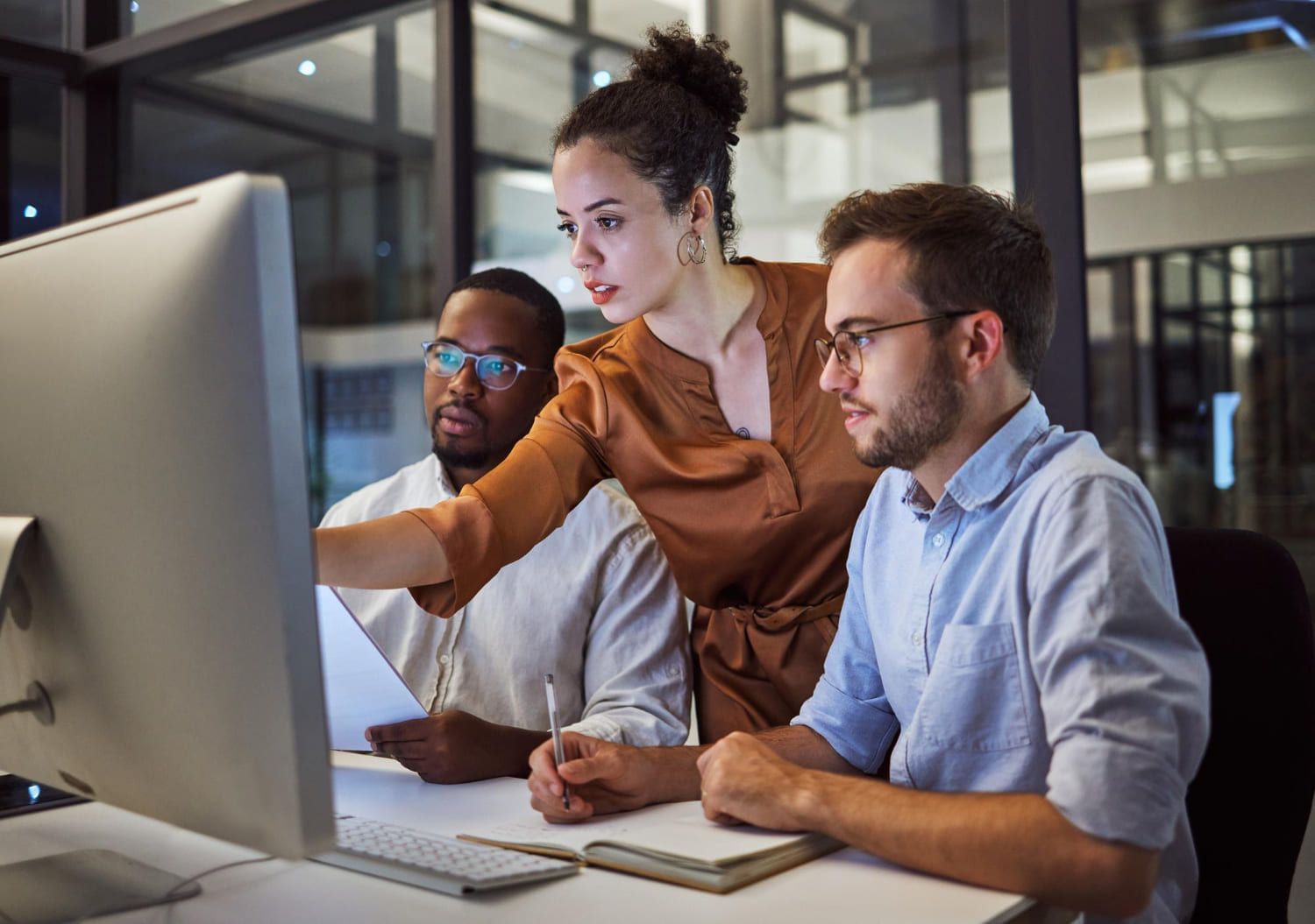 Mulher ao lado de dois homens (um branco e outro negro) aponta para a tela do computador; Profissões com maior crescimento de emprego em 2024