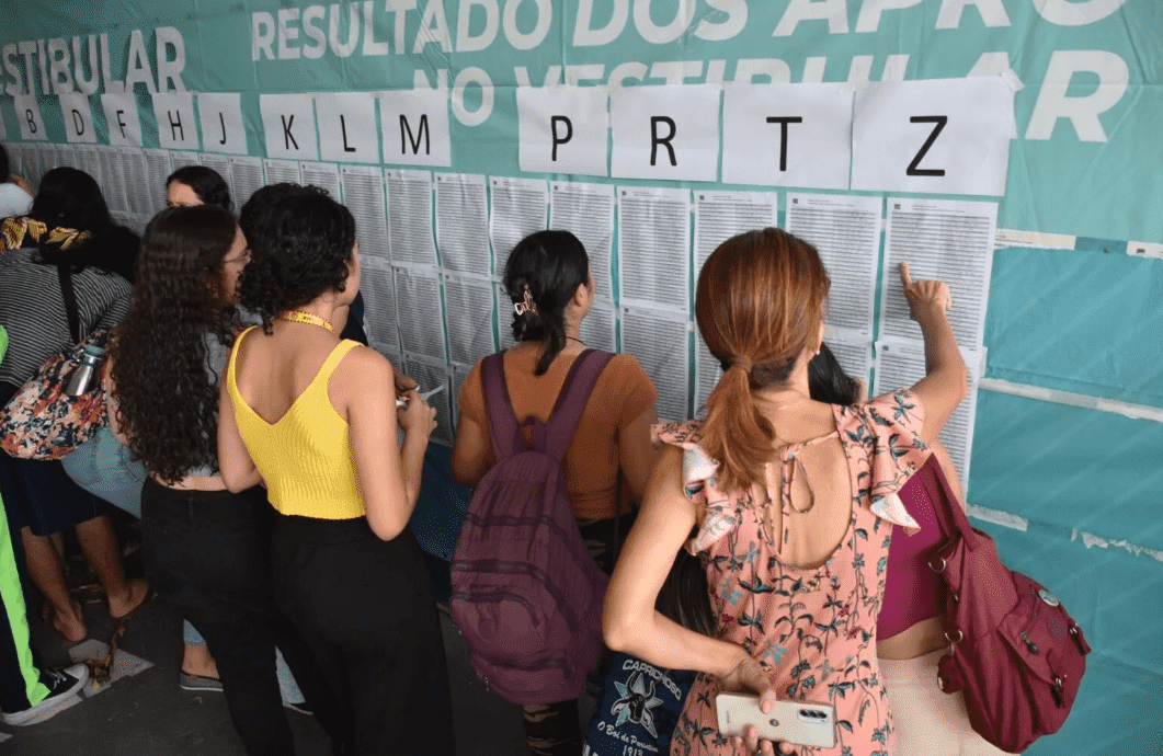 Mulheres na frente de um mural com lista de nomes pendurados; Como ver a lista de aprovados no Enem